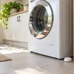 Water leak detector on a tile floor beside a washing machine in a bright laundry room